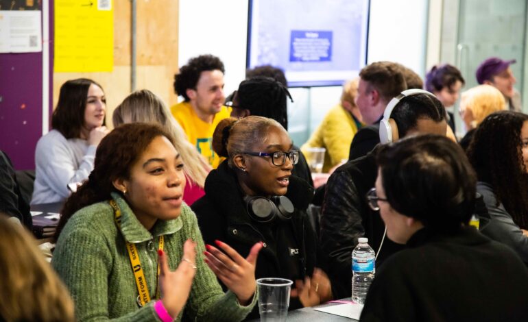 Young people at a mentors event talking across desks with their mentors.