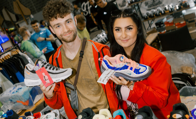 Two people holding sneakers whilst at a sneaker convention.