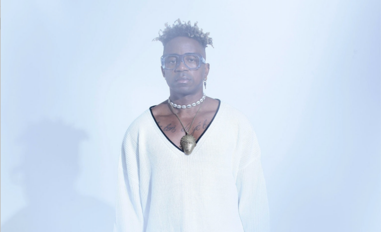 Blick Bassy posing in front of a white background in a white shirt.