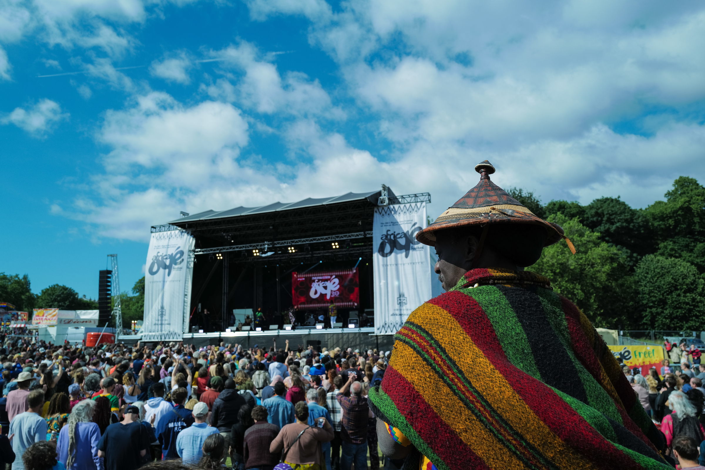 A crowd at a festival with a stage in the background and a person in traditional dress in the foreground.